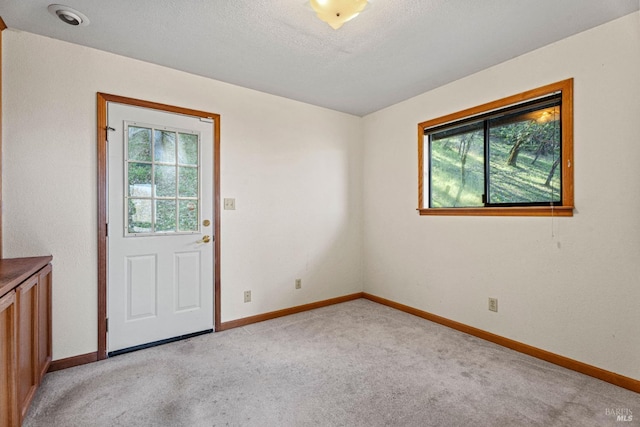 empty room featuring light colored carpet, baseboards, and a textured ceiling