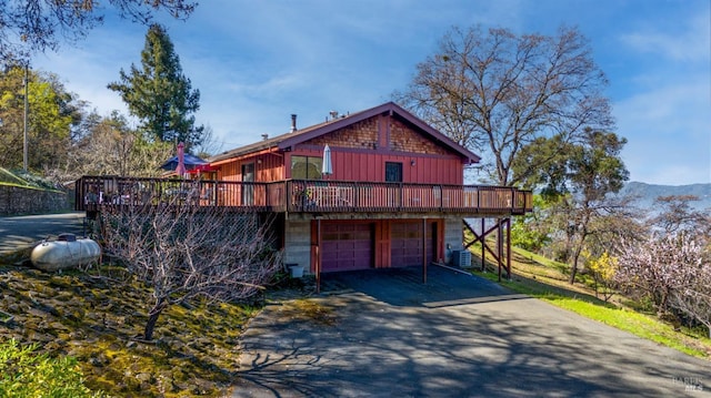 chalet / cabin featuring a deck with mountain view, cooling unit, driveway, and an attached garage