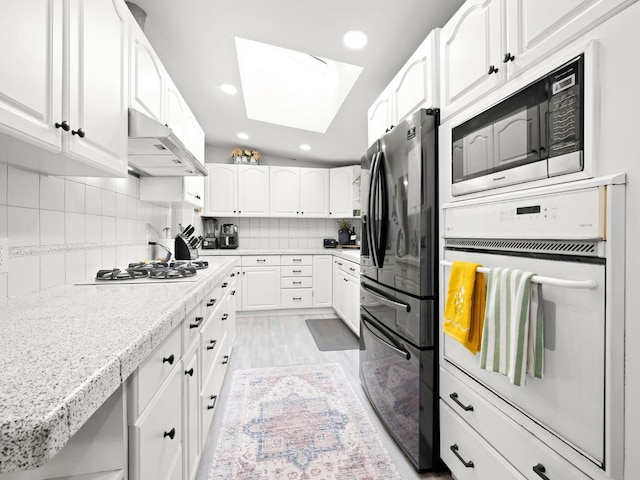 kitchen featuring white appliances, a skylight, white cabinets, under cabinet range hood, and tasteful backsplash