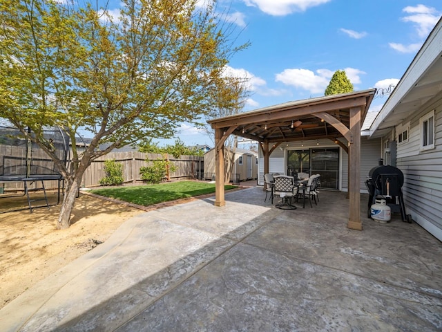 view of patio with outdoor dining space, a fenced backyard, an outdoor structure, a storage shed, and a trampoline