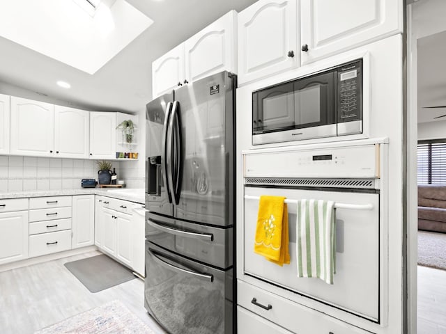 kitchen with backsplash, appliances with stainless steel finishes, light countertops, and white cabinetry