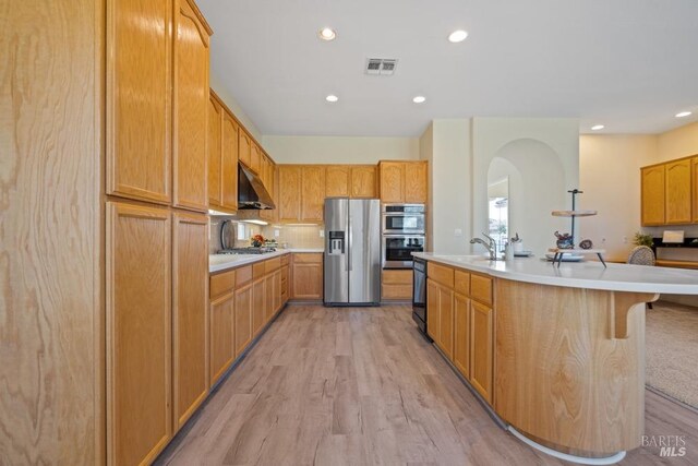 kitchen with exhaust hood, light wood-style floors, visible vents, appliances with stainless steel finishes, and arched walkways