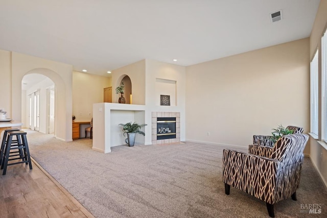 living room featuring arched walkways, a tile fireplace, visible vents, and baseboards