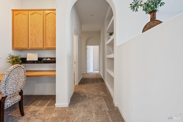 hall with carpet floors, built in features, arched walkways, and baseboards