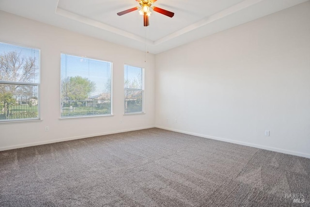carpeted empty room featuring plenty of natural light, a tray ceiling, baseboards, and ceiling fan