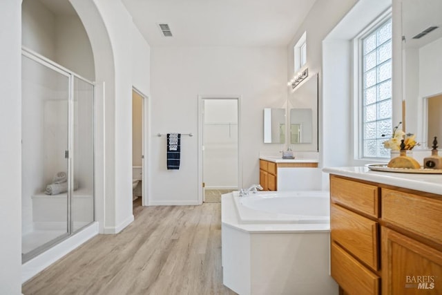 bathroom with two vanities, a shower stall, visible vents, a garden tub, and wood finished floors