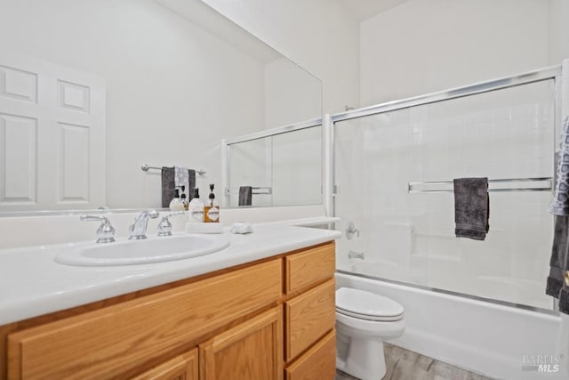 bathroom featuring toilet, wood finished floors, vanity, and enclosed tub / shower combo