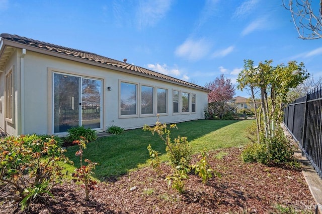 rear view of property featuring a yard, a tiled roof, fence, and stucco siding