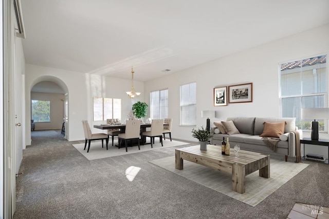 living room with arched walkways, a notable chandelier, and carpet floors
