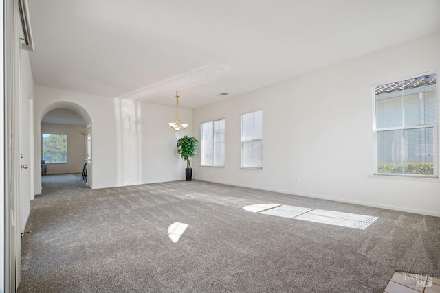 empty room with carpet floors, baseboards, arched walkways, and a chandelier