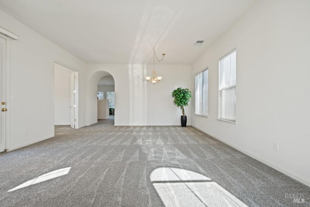 spare room featuring baseboards, an inviting chandelier, carpet flooring, visible vents, and arched walkways