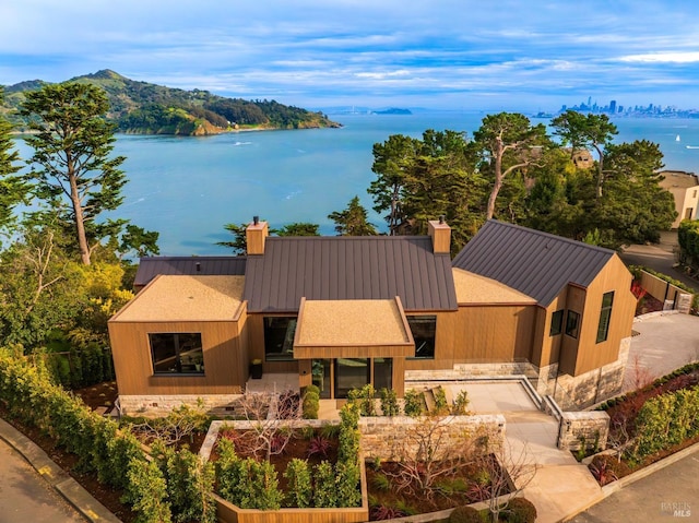 view of front of home with metal roof, a water view, a chimney, and a standing seam roof