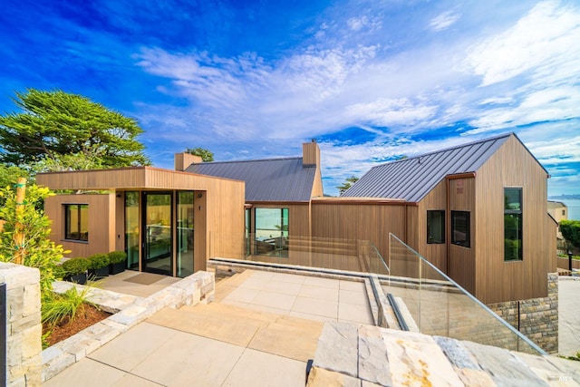 rear view of house with a chimney, a patio, metal roof, and a standing seam roof