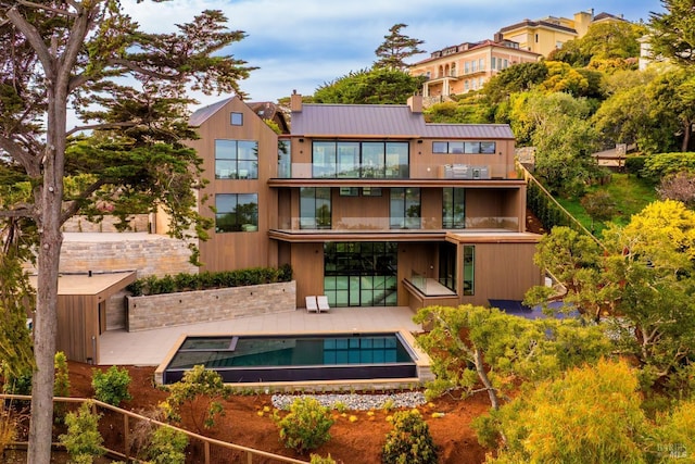 back of house featuring a standing seam roof, a patio, metal roof, a fenced in pool, and a chimney