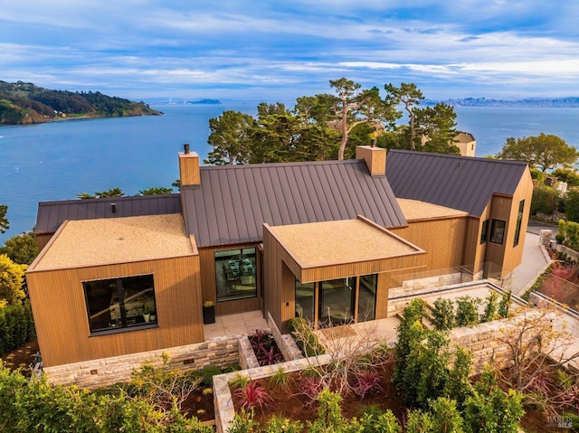 view of front of home with a standing seam roof, metal roof, a water view, and a chimney