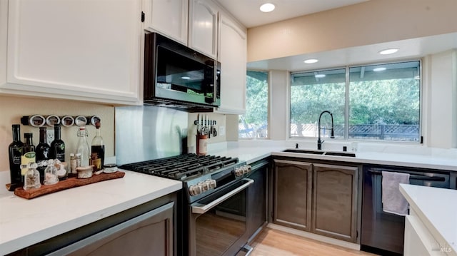 kitchen with a sink, white cabinetry, stainless steel appliances, light wood-style floors, and light countertops