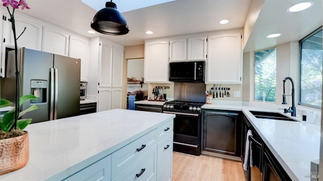 kitchen featuring a sink, white cabinetry, stainless steel appliances, light wood-style floors, and hanging light fixtures