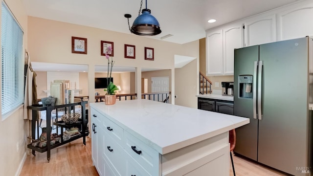 kitchen with stainless steel fridge with ice dispenser, light countertops, white cabinets, light wood-type flooring, and a center island