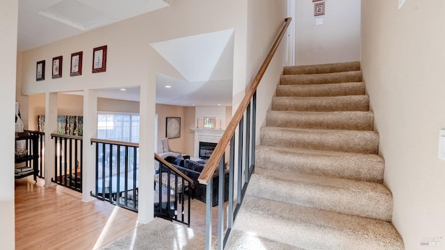 staircase with a glass covered fireplace, recessed lighting, and wood finished floors