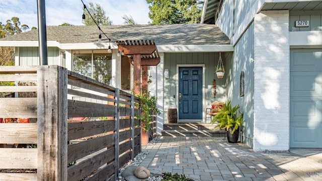 view of exterior entry with an attached garage, board and batten siding, and roof with shingles