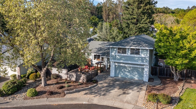 view of front facade with a shingled roof, concrete driveway, a garage, and fence
