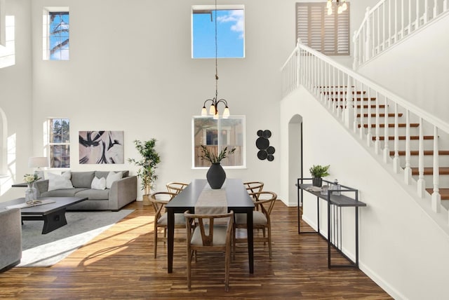 dining room featuring stairway, wood finished floors, a chandelier, and a towering ceiling