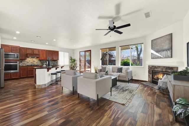 living area with visible vents, plenty of natural light, a fireplace, and dark wood-type flooring