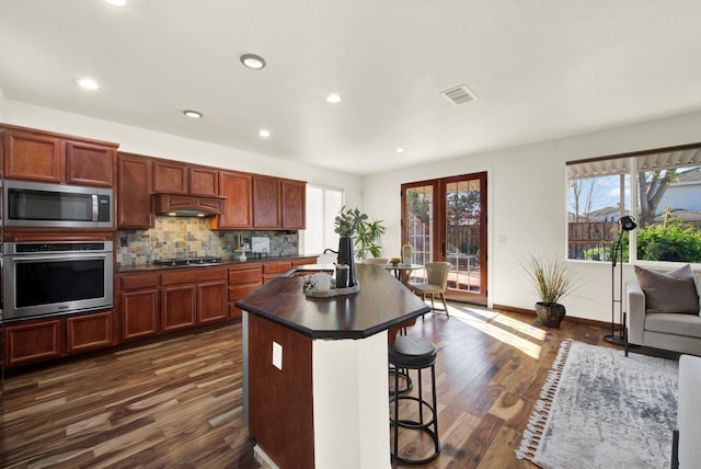 kitchen featuring dark countertops, visible vents, custom exhaust hood, stainless steel appliances, and a sink