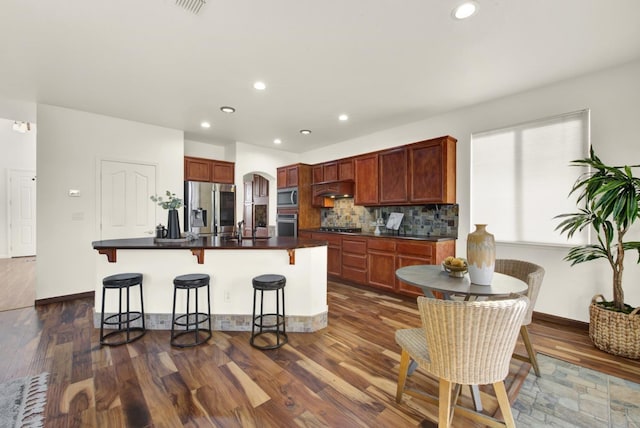 kitchen featuring under cabinet range hood, dark countertops, arched walkways, and appliances with stainless steel finishes