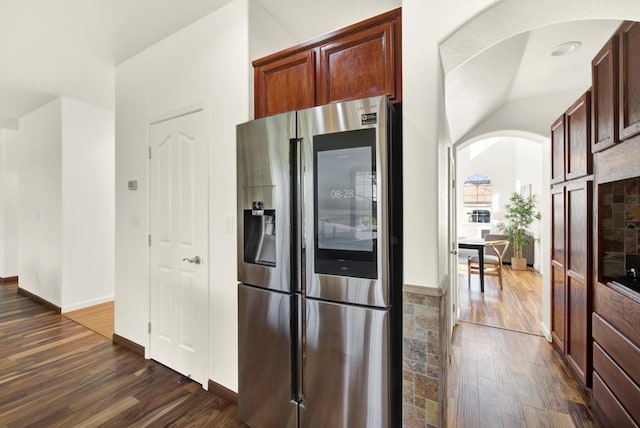 kitchen with arched walkways, baseboards, dark wood-type flooring, and stainless steel refrigerator with ice dispenser