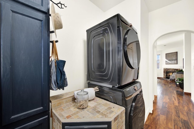 washroom with dark wood-style floors, a fireplace, baseboards, and stacked washer and dryer