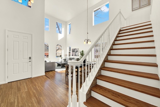 foyer entrance with stairs, a high ceiling, a notable chandelier, and wood finished floors