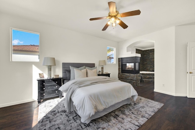 bedroom featuring ceiling fan, a multi sided fireplace, baseboards, and wood finished floors