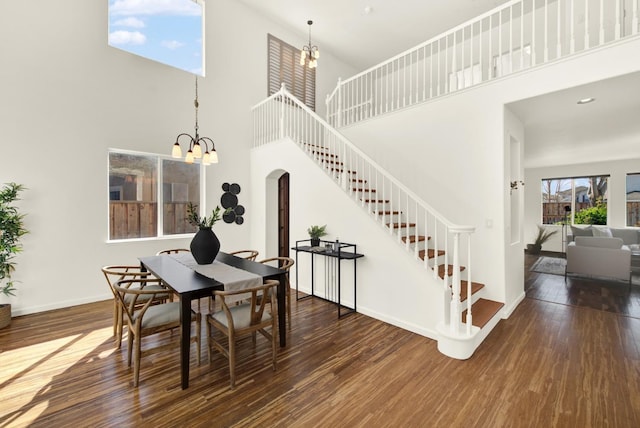 dining space featuring baseboards, stairs, hardwood / wood-style floors, a towering ceiling, and a notable chandelier