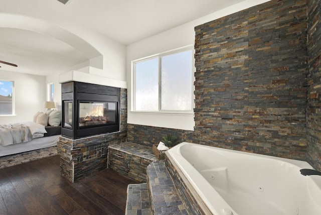 ensuite bathroom featuring ensuite bathroom, hardwood / wood-style flooring, a multi sided fireplace, ceiling fan, and a whirlpool tub