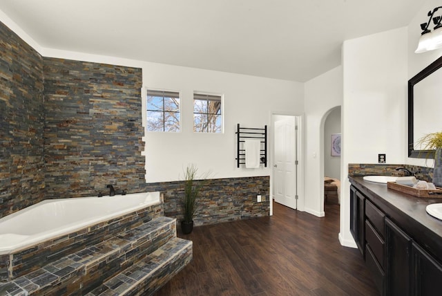 full bathroom featuring a bath, double vanity, wood finished floors, and a sink