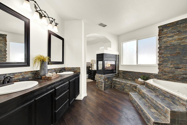 full bath featuring a sink, visible vents, a multi sided fireplace, and plenty of natural light