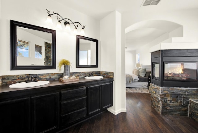 ensuite bathroom featuring a sink, visible vents, a stone fireplace, and wood finished floors