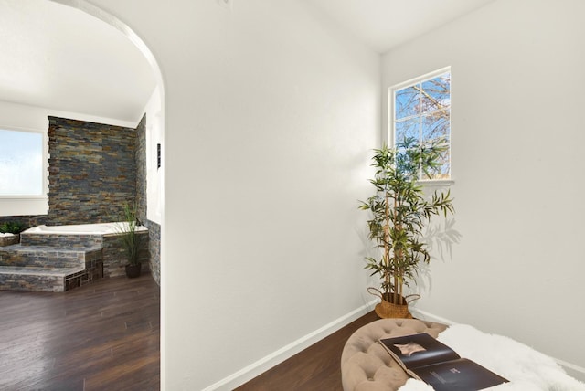 corridor with wood finished floors, arched walkways, a wealth of natural light, and baseboards