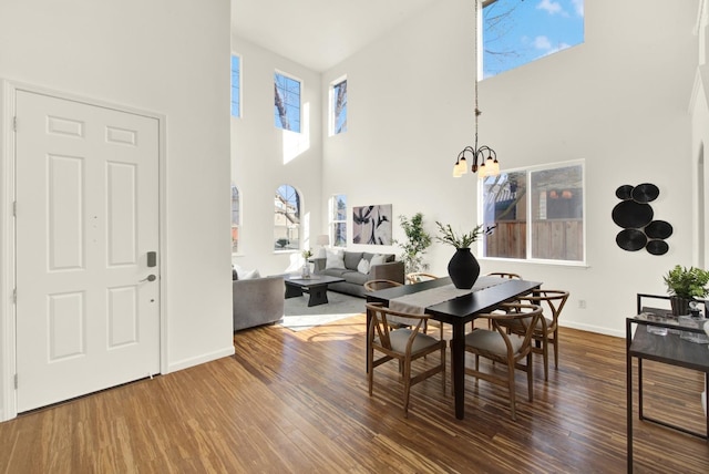 dining space featuring baseboards, a notable chandelier, a high ceiling, and wood finished floors