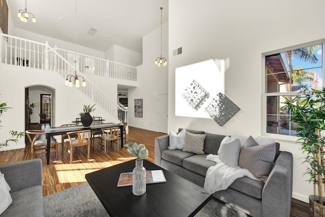 living area with visible vents, dark wood finished floors, stairway, a high ceiling, and an inviting chandelier