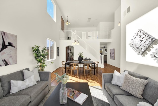 living area with arched walkways, visible vents, a high ceiling, and wood finished floors