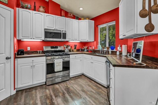 kitchen with a sink, recessed lighting, appliances with stainless steel finishes, white cabinets, and lofted ceiling