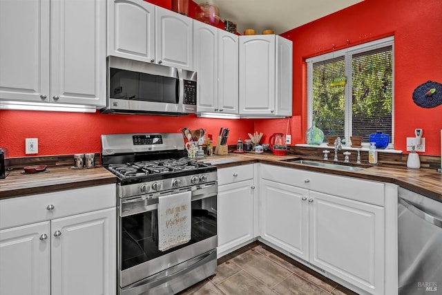 kitchen featuring white cabinets, appliances with stainless steel finishes, butcher block counters, and a sink