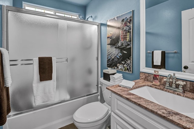 full bath featuring vanity, toilet, a textured wall, and combined bath / shower with glass door