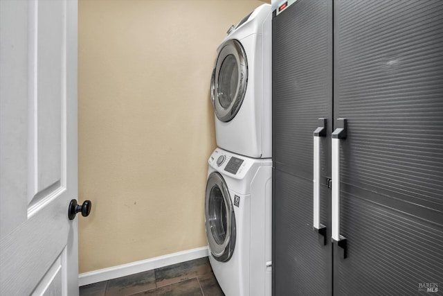 laundry room featuring laundry area, dark tile patterned floors, baseboards, and stacked washer and clothes dryer