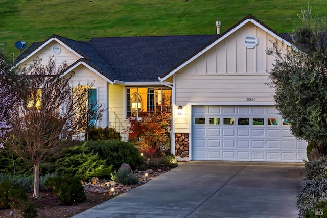 view of front of property featuring a shingled roof, concrete driveway, a garage, stone siding, and board and batten siding