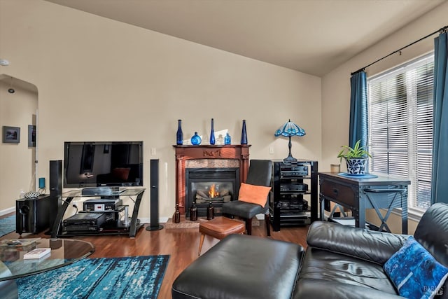 living room with a fireplace, wood finished floors, arched walkways, and baseboards