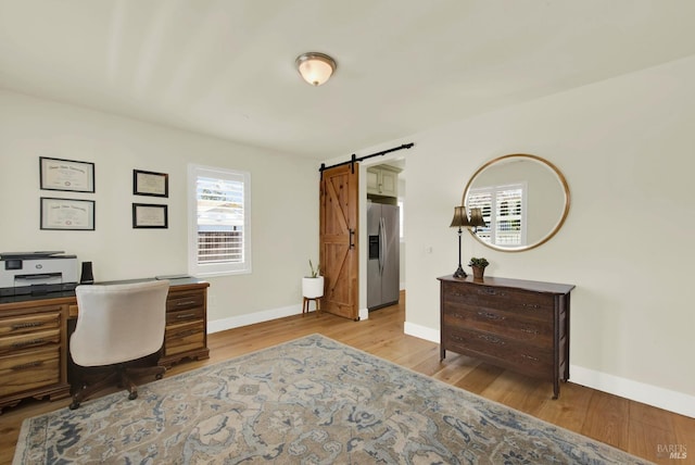 office area featuring a barn door, light wood-style floors, and baseboards