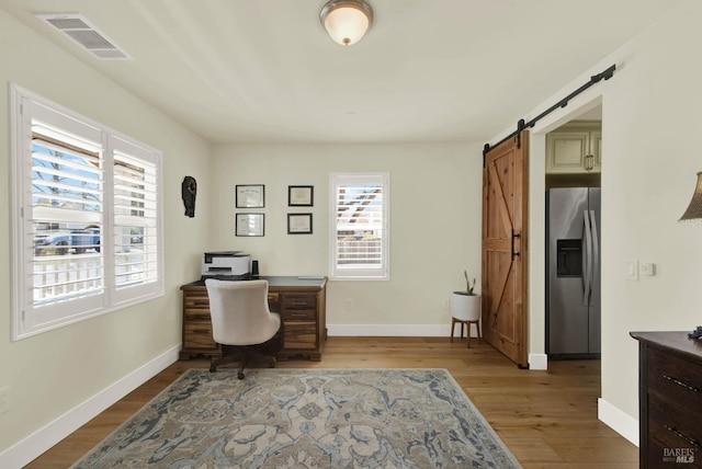 office area featuring visible vents, a barn door, light wood-style floors, and baseboards